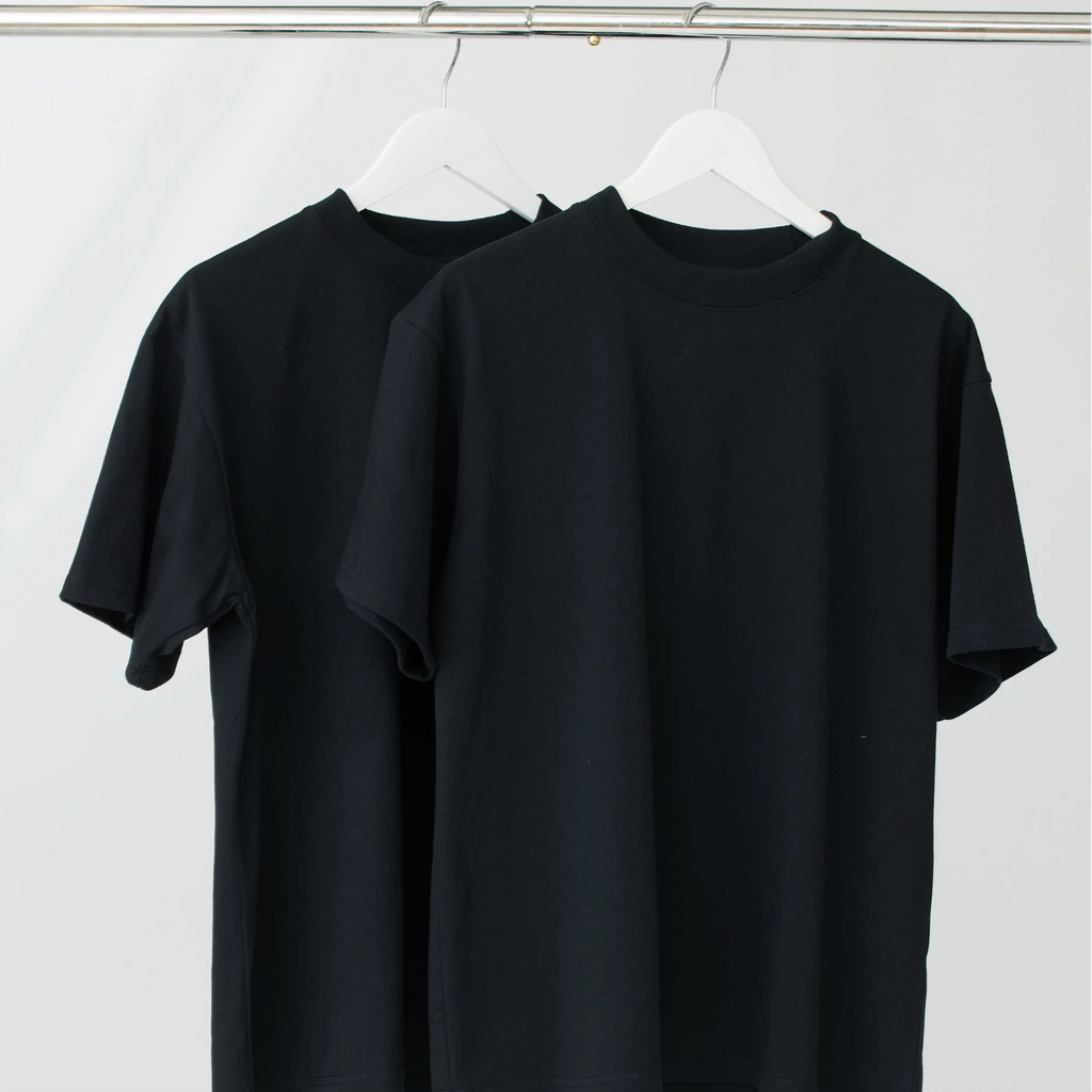 Two black t-shirts hanging on a white wall.