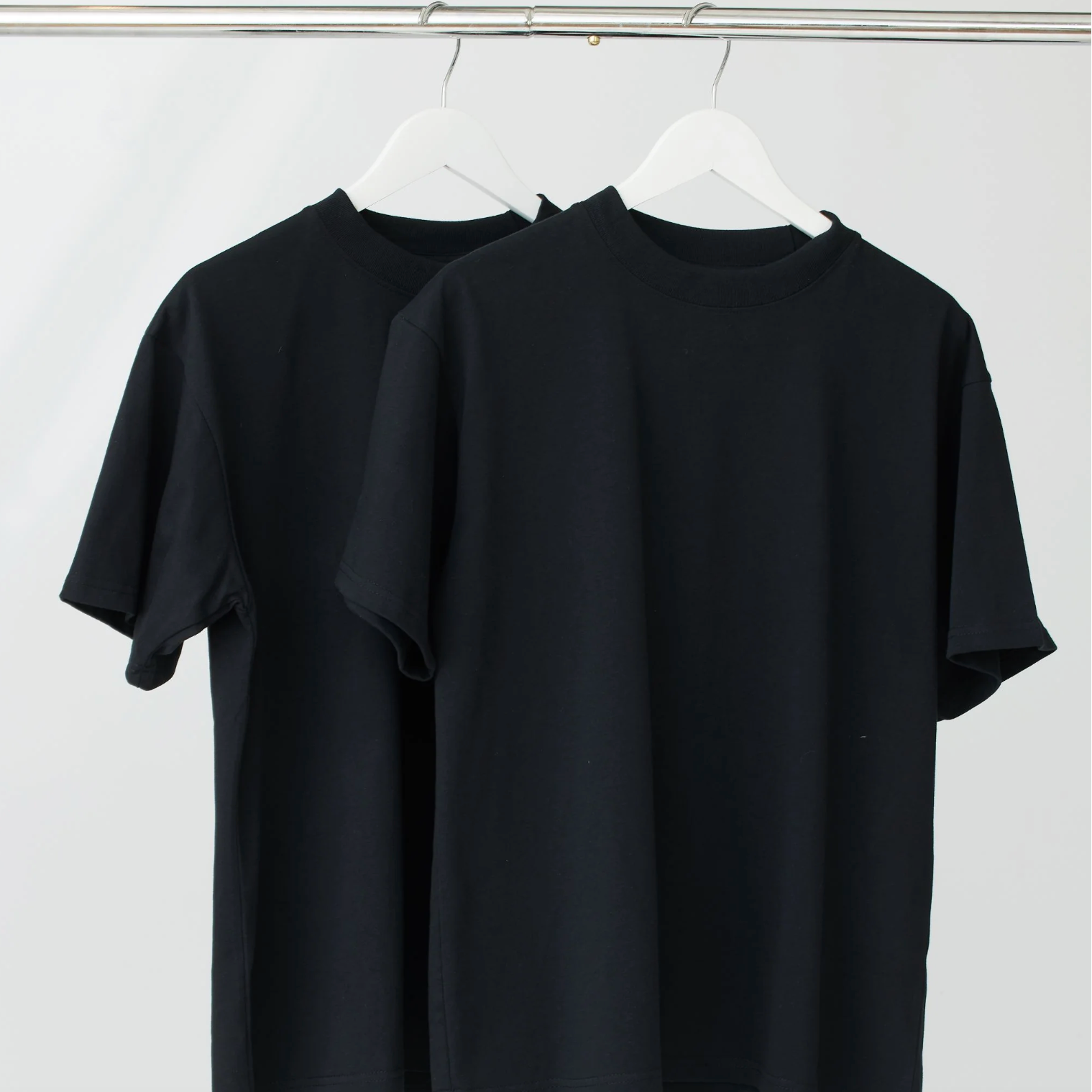 Two black t-shirts hanging on a white wall.